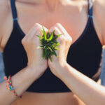 Close-up of a person holding fresh cannabis leaves in a heart-shaped gesture, symbolizing wellness and mindfulness.