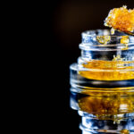 Macro shot of golden cannabis concentrate being scooped from a glass jar, showcasing its rich texture.