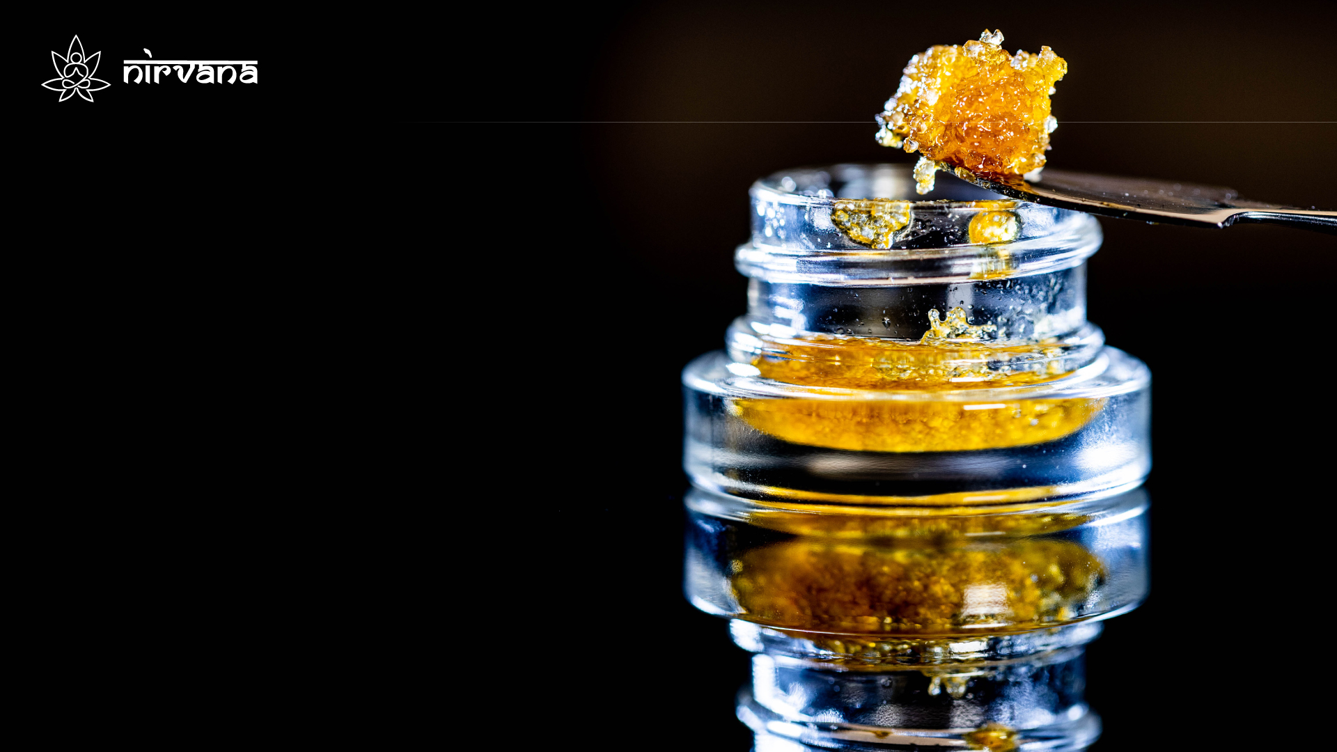 Macro shot of golden cannabis concentrate being scooped from a glass jar, showcasing its rich texture.